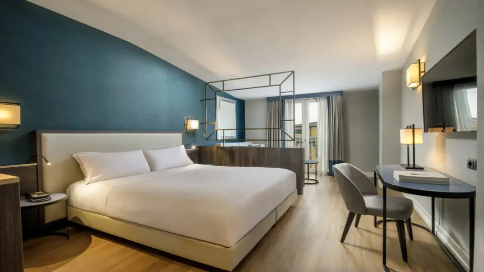 A calm guest room with a white bed, a deep teal feature wall and a small desk by the window.